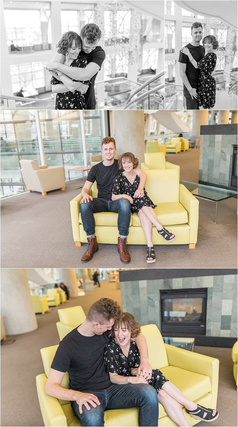 A cute couple inside of a modern building. The couple is hugging, and laughing. They are sitting on a yellow couch, laughing.