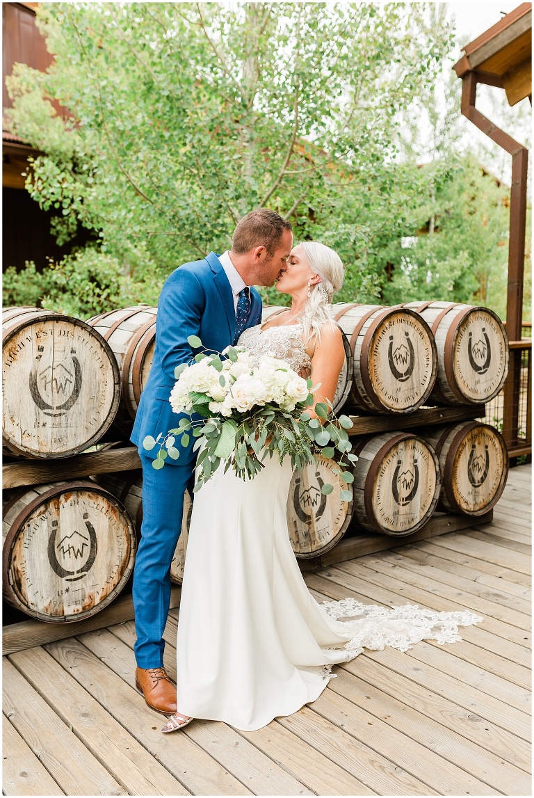Husband and wife kissing in front of whiskey barrells