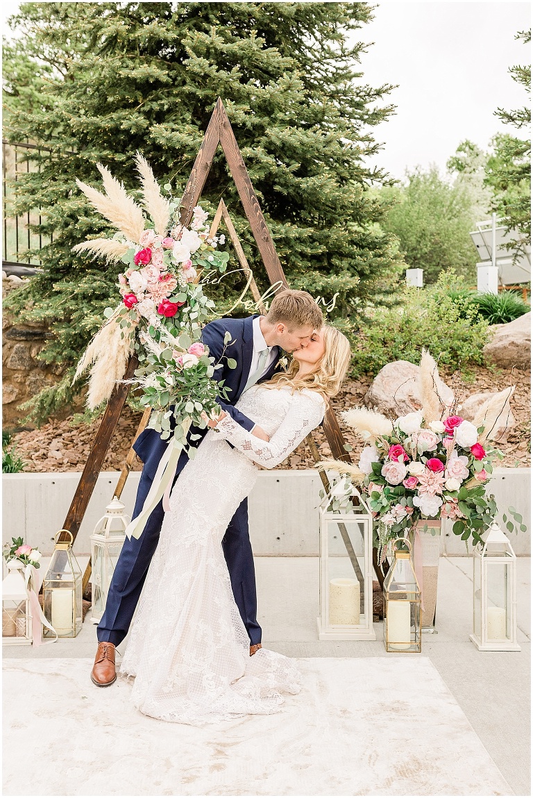 Husband and Wife kissing in front of triangle Wedding Arch